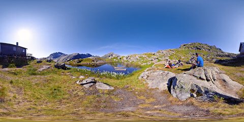 Hikers Sitting By Lake Near Mountain Hut
