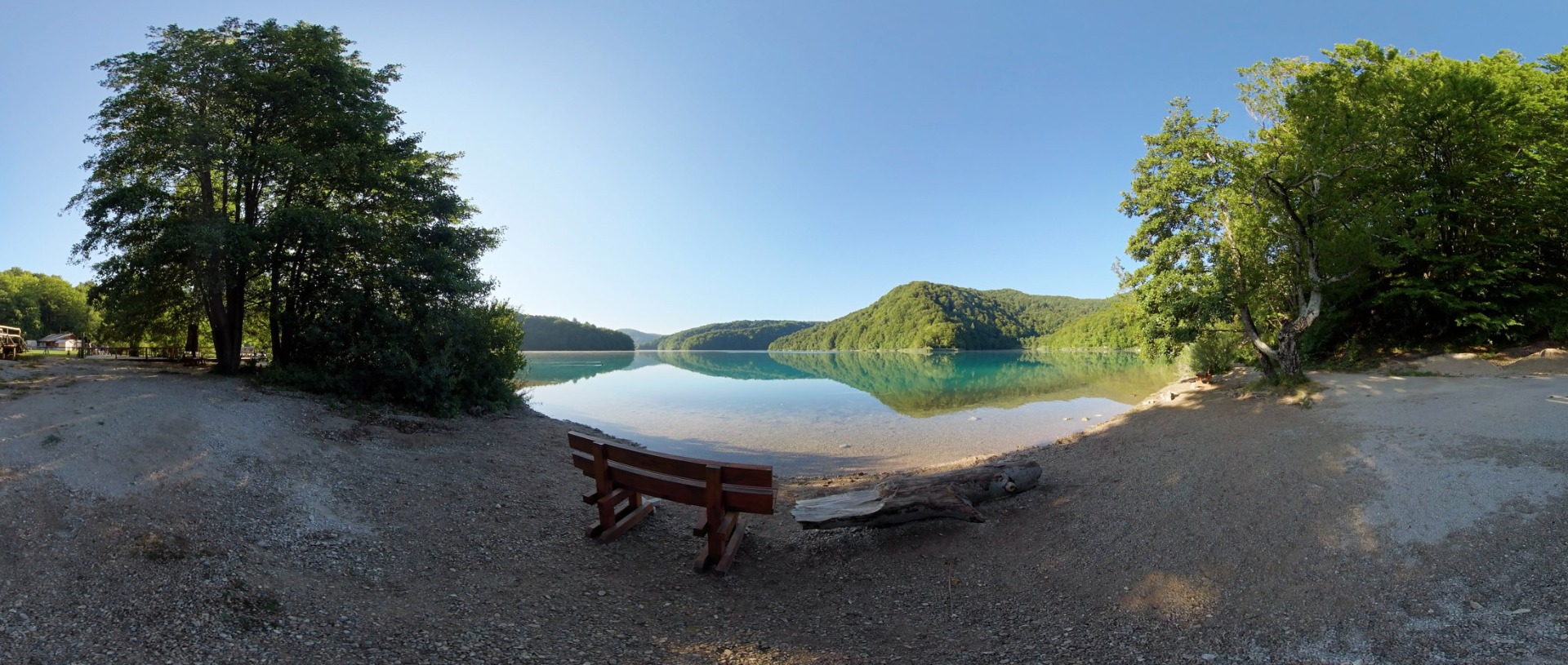 Calm turquoise lake ringed by forested hills, viewed from the shore